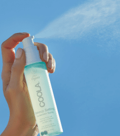 en hånd, der holder en flaske spray mod en blå himmel.