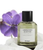 en flaske parfume, der sidder ved siden af en lilla blomst.