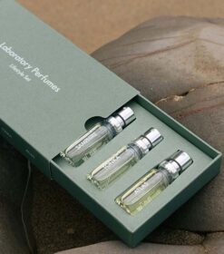 Tre Laboratory Parfums Discover sæt, som hver indeholder 5x 5 ml parfumeflasker, i en grøn boks på en sten.