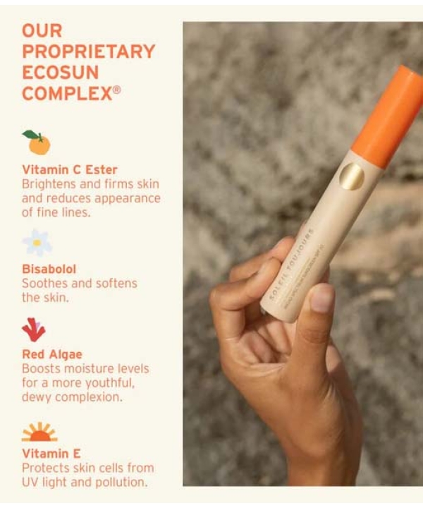 En hånd holder et Soleil Toujours Mineral Ally Eye Glow + Illuminator SPF 30 ml produkt med en orange hætte. Teksten til venstre viser ingredienser: C-vitaminester, Bisabolol, Rødalger og E-vitamin, der fremhæver deres fordele for hudpleje.