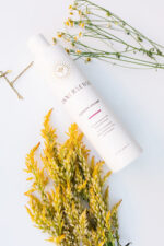 En flaske Innersense I Create Volume - Volumizing Lotion 295ml med gule blomster ved siden af.