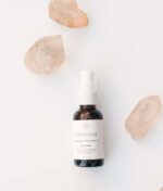 En flaske Innersense Harmonic Healing & Treatment Oil Skin, Scalp & Hair 25ml placeres på en hvid overflade omgivet af tre gennemskinnelige krystaller.