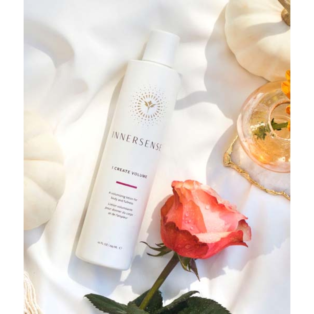 En flaske Innersense I Create Volume - Volumizing Lotion 295ml liggende ved siden af en rose og et græskar.
