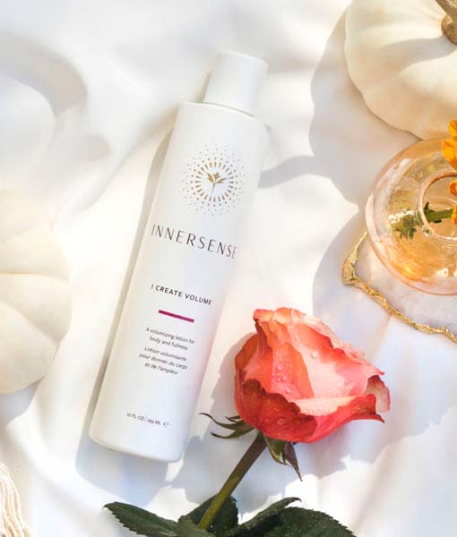 En flaske Innersense I Create Volume - Volumizing Lotion 295ml liggende ved siden af en rose og et græskar.