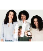 Tre kvinder med krøllet hår holder forskellige hårplejeprodukter frem, inklusive Innersense Hydrating Cream Hairbath - Dry & Thirsty hair (sulfatfri) 295ml, smilende til kameraet.
