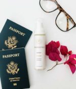 To amerikanske pas, briller, en flaske Innersense Refresh Dry Shampoo - Skum til pulver 70 ml og lyserøde bougainvillea blomster mod en hvid baggrund.