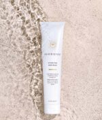Innersense Hydrating Hair Mask - Repair & Revitalize 177 ml tuben hviler på en tekstureret overflade med rislende vand i nærheden, hvilket fremhæver dens naturlige essens. Designet til at reparere og fugte håret og indeholder certificerede økologiske ingredienser til nærende behandling.