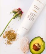 Tube of Innersense Hydrating Hair Mask - Repair & Revitalize 177ml, en halv avocado, en blomst, en krystal og noget plantemateriale vist på en lys baggrund.