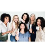 En gruppe på seks smilende kvinder i forskellige aldre og hårtyper, der holder Innersense Hydrating Cream Conditioner - Dry & Thirsty Hair 295ml, stående sammen mod en almindelig hvid baggrund.