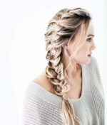 Sideprofil af en kvinde med en løs fiskehalefletning i sit blonde hår, perfekt stylet med Innersense I Create Finish - Shine Spray 295ml. Hun er iført en lysegrå, off-the-shoulder strikket sweater. Baggrunden er almindelig hvid.