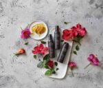 tre flasker bodylotion siddende på en bakke ved siden af blomster.