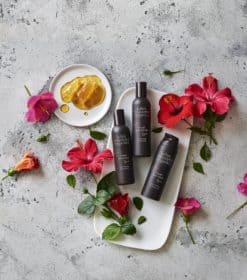 tre flasker bodylotion siddende på en bakke ved siden af blomster.