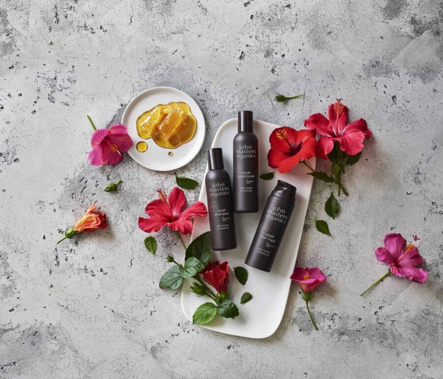 tre flasker bodylotion siddende på en bakke ved siden af blomster.