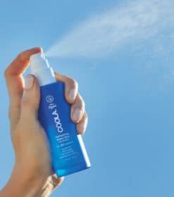 en hånd, der holder en flaske deodorantspray mod en blå himmel.
