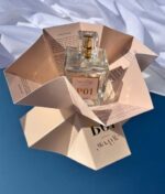 En flaske parfume mærket "Ærlig P01 - Eau de Parfum 100 ml glasflaske" står på et foldet papstander med produktinformation, sat mod en blå og hvid baggrund.