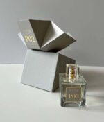 En flaske parfume mærket "Ærlig P02 - Eau de Parfum 100 ml glasflaske" placeres på en hvid overflade ved siden af dens åbne, grå geometriske emballage.