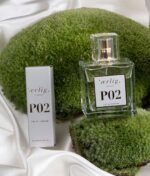 En klar flaske Ærlig P02 - Eau de Parfum 100 ml glasflaske og dens emballage er udstillet på grønt mos med hvid satinbagtæppe.
