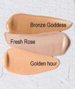 Swatches af tre makeup nuancer mærket: "Bronze Goddess", "Fresh Rose" og "COOLA Mineral Rōsilliance® Tinted Moisturizer sunscreen - Golden hour SPF 30 44ml" på en tekstureret hvid baggrund.