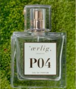 En flaske 'Ærlig P04 Eau de Parfum 100 ml glasflaske' med et klart glasdesign og guldfarvet dyse, placeret på en grøn tekstureret overflade.