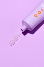 en tube lotion, der sidder oven på en lyserød overflade.