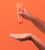 en hånd, der holder et rør med orangefarvet gel.