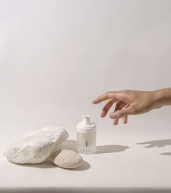 en hånd, der rækker ud efter en flaske lotion ved siden af en sten.