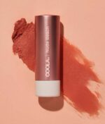 COOLA Mineral Liplux® SPF30 - Nude Beach mod en baggrund med en udtværing af balsamens farve.