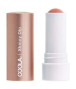 En tube COOLA Mineral Liplux® Tinted Lip Balm SPF 30 - Skinny Dip med en åben roseguldhætte, der afslører en koralfarvet balsamstick inde i en hvid base.