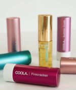 Der vises en række COOLA-produkter, herunder rør mærket Firecracker og Summer Crush, og en flaske COOLA Mineral Liplux® SPF30 - Nude Beach.