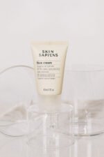 En tube Skin Sapiens Face Cream 40 ml siddende oven på et glas.