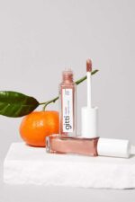 en flaske lipglosser ved siden af en appelsin.