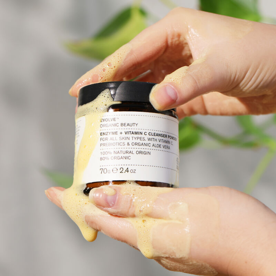 en persons hånd, der holder en krukke med Evolve Organic Beauty Enzyme + Vitamin C Cleansing Powder 70 g creme.