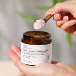 en hånd, der holder en krukke med Evolve Organic Beauty Enzyme + Vitamin C Cleansing Powder 70 g.
