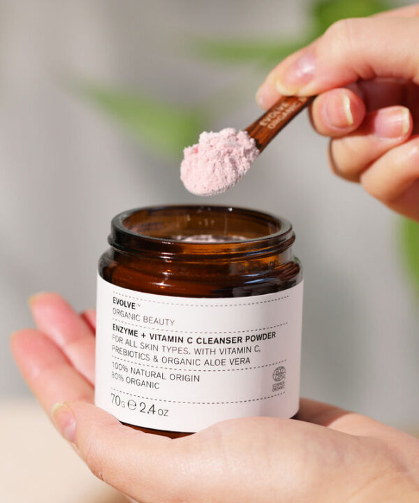 en hånd, der holder en krukke med Evolve Organic Beauty Enzyme + Vitamin C Cleansing Powder 70 g.