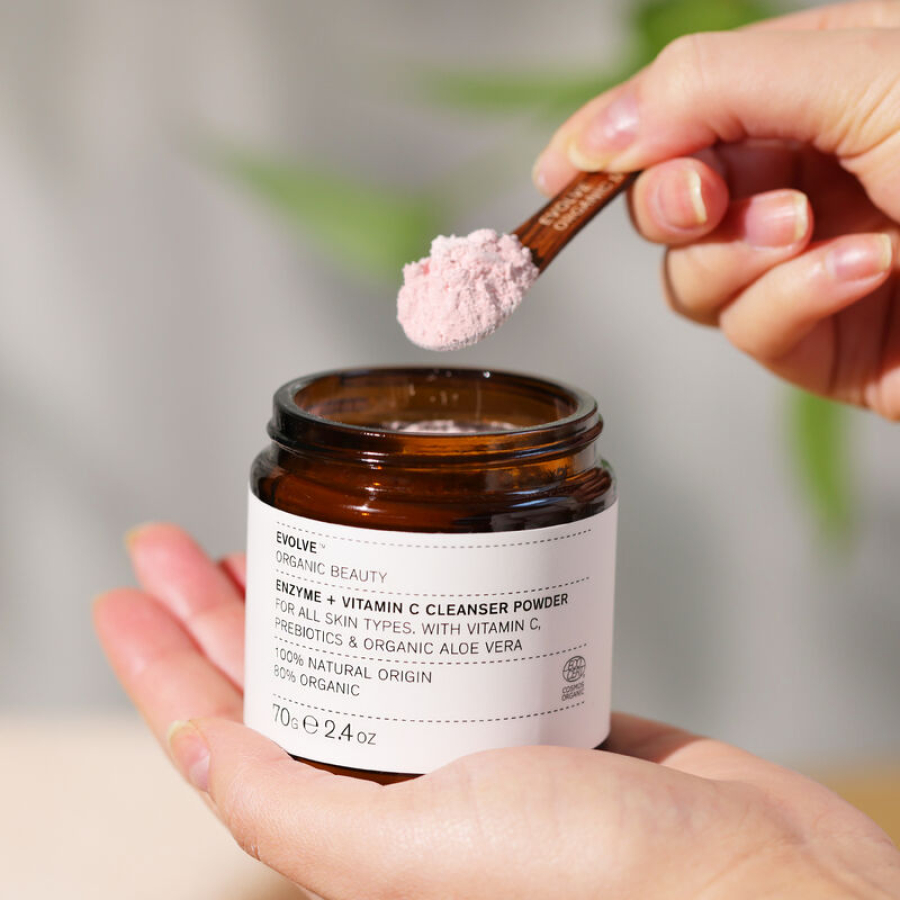 en hånd, der holder en krukke med Evolve Organic Beauty Enzyme + Vitamin C Cleansing Powder 70 g.