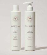 To hvide flasker med Innersense hårplejeprodukter vises: den ene mærket "Clarity Hairbath" og den anden "Clarity Conditioner", begge med et minimalistisk design. Sammen danner de Innersense Clear + Calm Clarity Duo - Hairbath & Conditioner for en rolig hårplejeoplevelse.