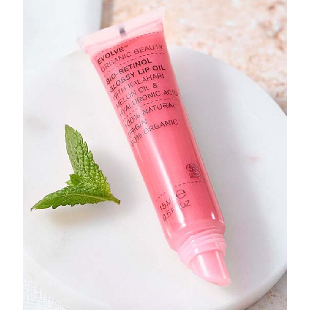 En tube Evolve Organic Beauty Bio-Retinol Glossy Lip Oil 15 ml med et mynteblad ved siden af.