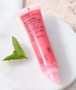 En tube Evolve Organic Beauty Bio-Retinol Glossy Lip Oil 15 ml med et mynteblad ved siden af.