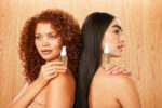 To kvinder holder en flaske Innersense Hair Renew Scalp Oil 29 ml ved siden af hinanden.