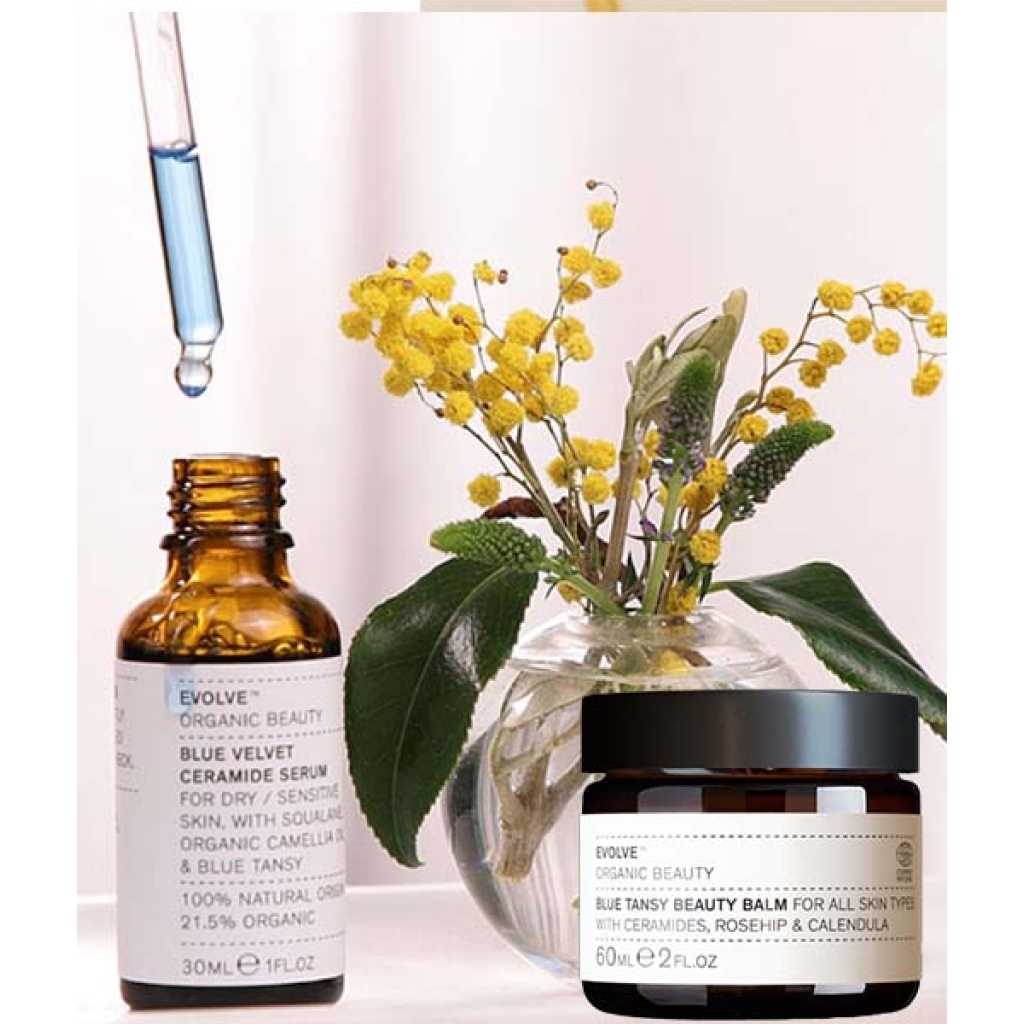 En flaske Evolve Blue Velvet Ceramide Serum & Blue Tansy Beauty Balm sæt ved siden af en flaske gule blomster.