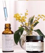 En flaske Evolve Blue Velvet Ceramide Serum & Blue Tansy Beauty Balm sæt ved siden af en flaske gule blomster.