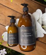 En flaske NAKED - Natural Haircare - Hårmaske nr. 1, 1000 ml siddende på et bord ved siden af blomster.