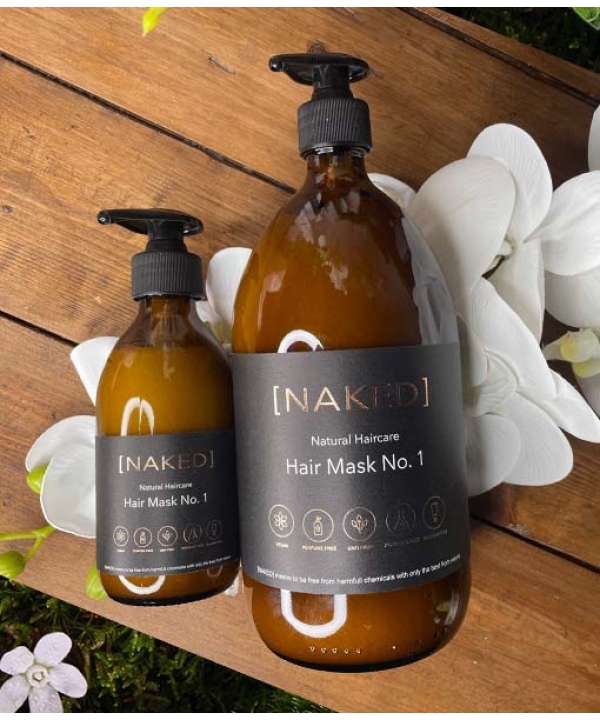 En flaske NAKED - Natural Haircare - Hårmaske nr. 1, 1000 ml siddende på et bord ved siden af blomster.