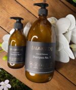 En flaske NAKED - Natural Haircare Tea Tree Shampoo, 1000 ml og en flaske vand på et træbord.
