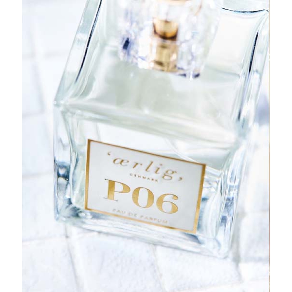 Klar glasflaske "Ærlig P06 – Eau de Parfum 15 ml glasflaske Roll on TRAVEL" med guldhætte og etiket, placeret på en hvid struktureret overflade.