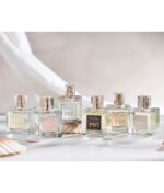 Seks flasker parfume med guldlåg mærket P01, P03, Ærlig P05 – Eau de Parfum 15 ml glasflaske Roll on TRAVEL, P04, P06 og P12 er anbragt på en lys overflade med muslingeskaller omkring.