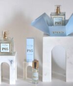 Udstilling af Ærlig P05 – Eau de Parfum 15 ml glasflaske Roll on TRAVEL flasker og æsker arrangeret på hvid marmor stativer med arkitektonisk buedesign.