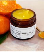 Krukke med Evolve Miracle Vitamin C Mask 60 ml med en skive appelsin og en ske indeholdende produkt på en marmoroverflade.
