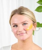 Kvinde med en Evolve Miracle Vitamin C Mask 60 ml plaster på kinden.