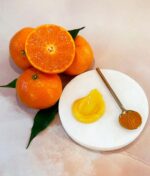 En gruppe hele og halverede Evolve Miracle Vitamin C-masker ved siden af en hvid tallerken med en klat appelsinmarmelade og en teske med lidt appelsinskal.